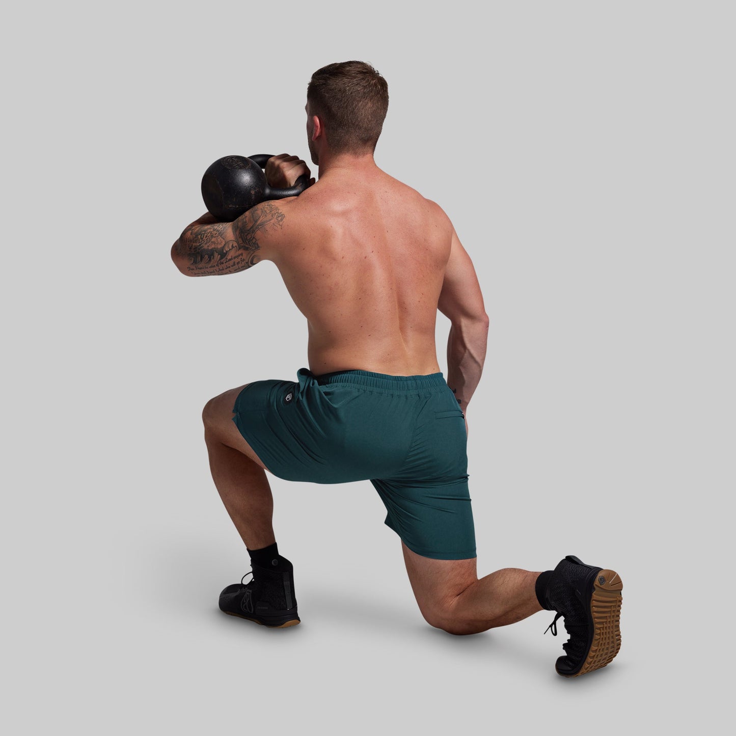 Man in green shorts and black boxing gloves performing a lunge on a gray background