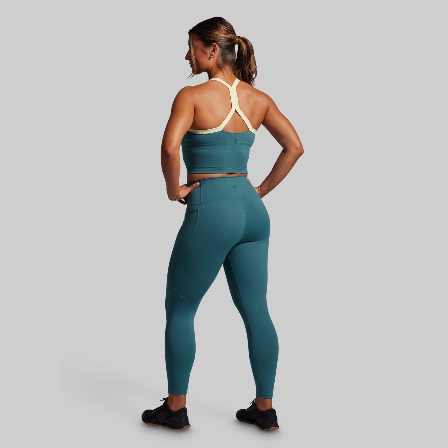Woman wearing a teal sports bra and leggings set on a gray background