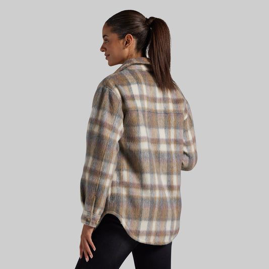 A woman shown from the back wearing a long-sleeve plaid button-up jacket. The shirt features a warm beige, brown, and cream plaid pattern.