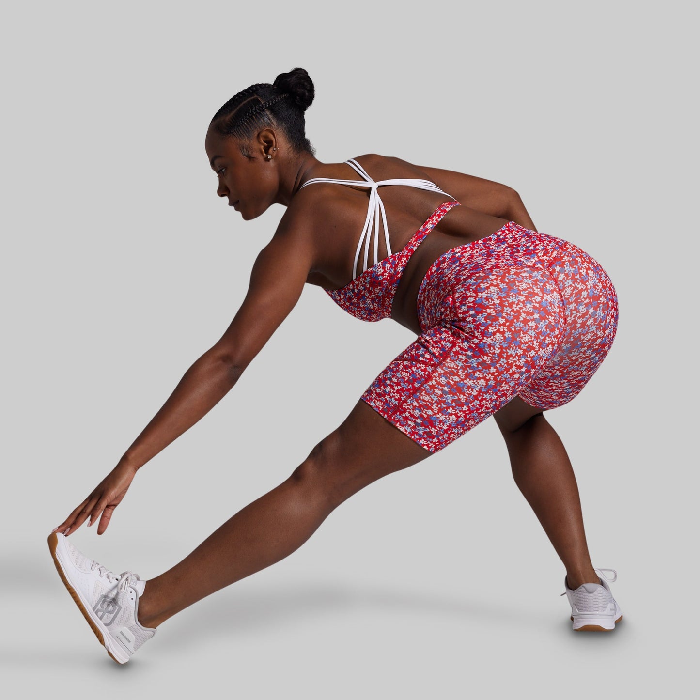Woman in a floral outfit stretching on a plain background