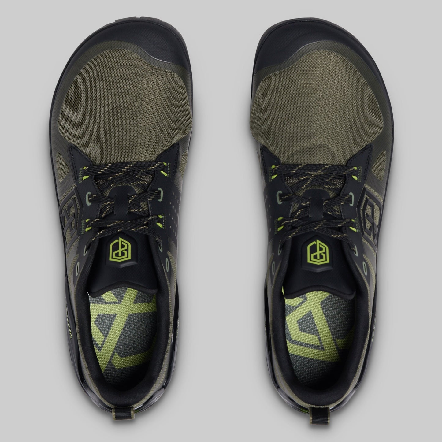 A pair of athletic minimalist training shoes shown from a top-down view on a light gray background. The shoes feature a black and olive green colorway with neon yellow-green accents on the laces, logo, and insole.
