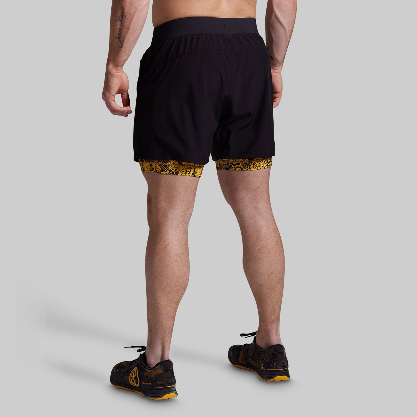 Person wearing black athletic shorts with a yellow pattern on a gray background