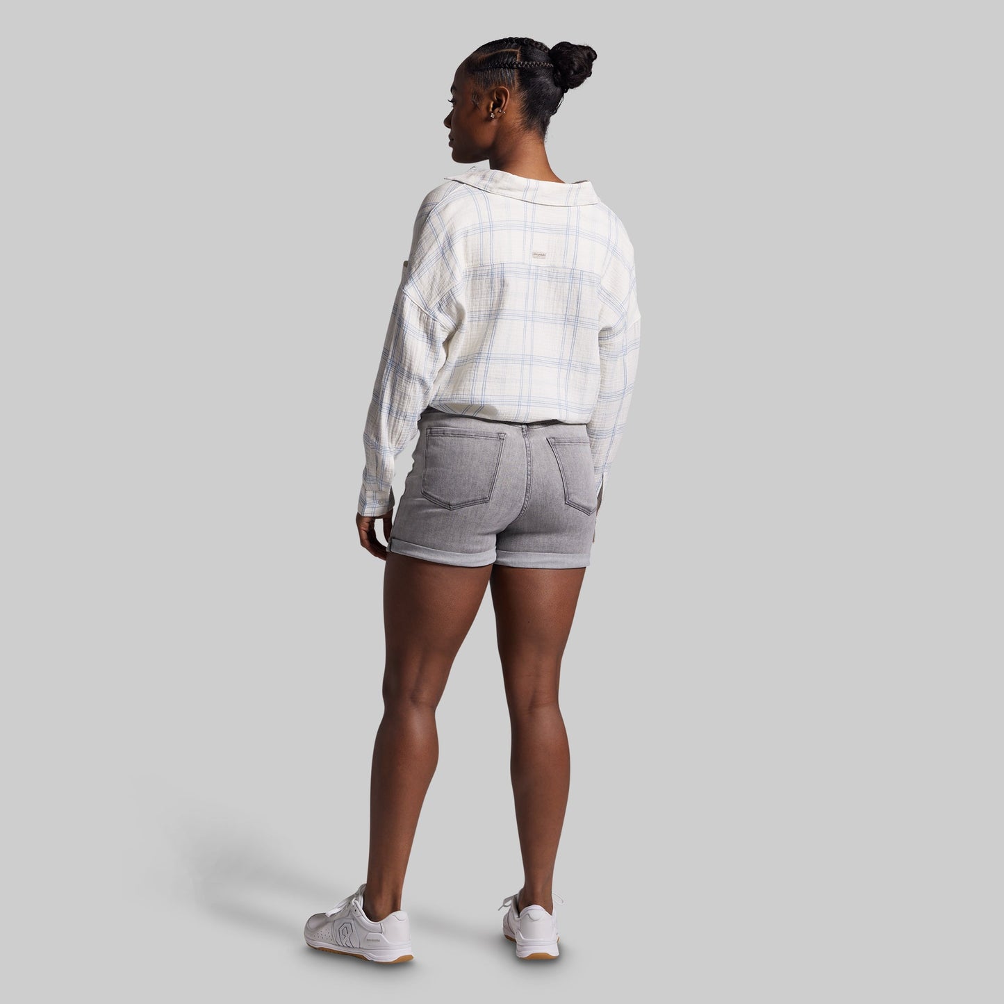 Person wearing a white plaid shirt and gray shorts on a light gray background