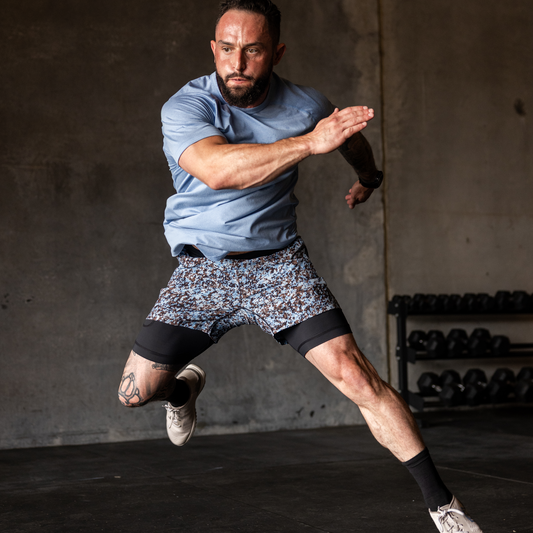 Man in athletic wear jumping in a gym setting with weights in the background