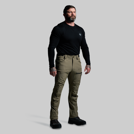 Man wearing a black long-sleeve shirt and green pants on a gray background