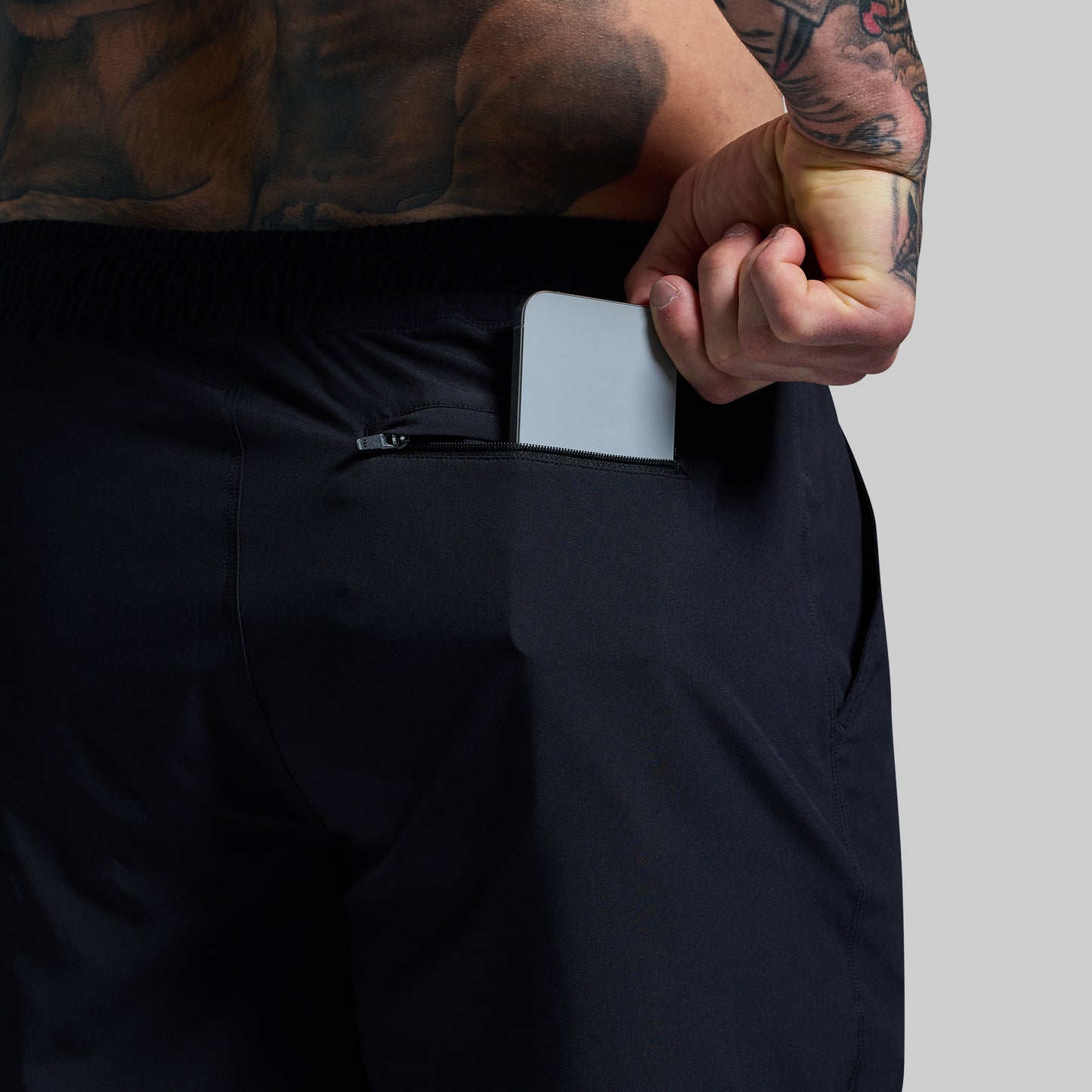 Person wearing black pants with a phone in the pocket against a gray background
