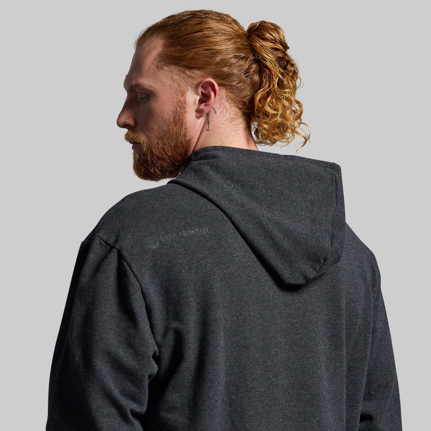 Man wearing a dark gray hoodie with a visible brand logo on the back against a plain background