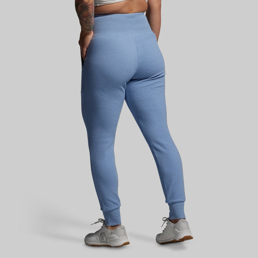 Person wearing blue textured joggers on a gray background