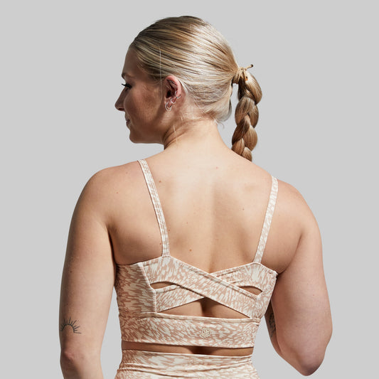 Woman wearing a beige patterned sports bra with cut-out design on a plain background