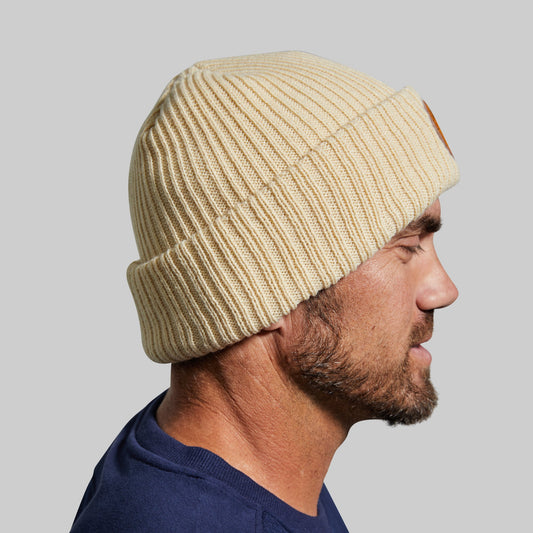 Side view of a man wearing a beige beanie against a gray background