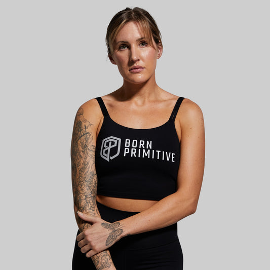 A woman wearing a black sports bra with the text 'BORN PRIMITIVE' on the front.