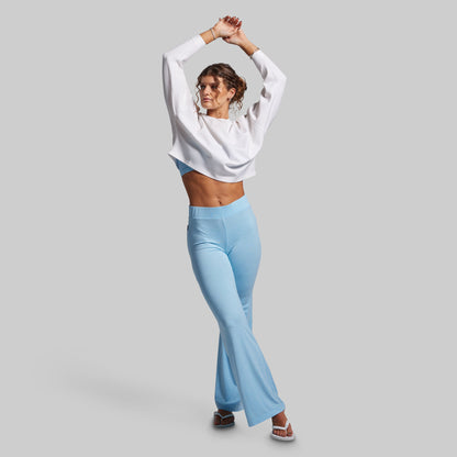Woman wearing a white sweatshirt and light blue flared pants on a gray background