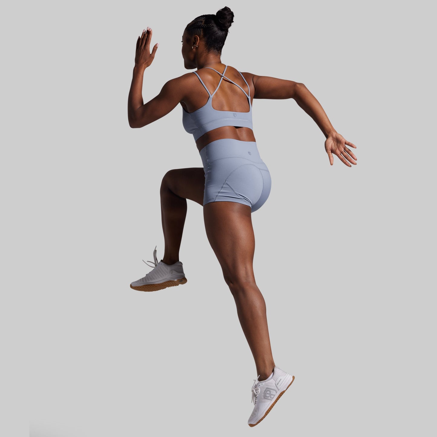 Person wearing a light blue sports bra and shorts set, jumping on a plain background