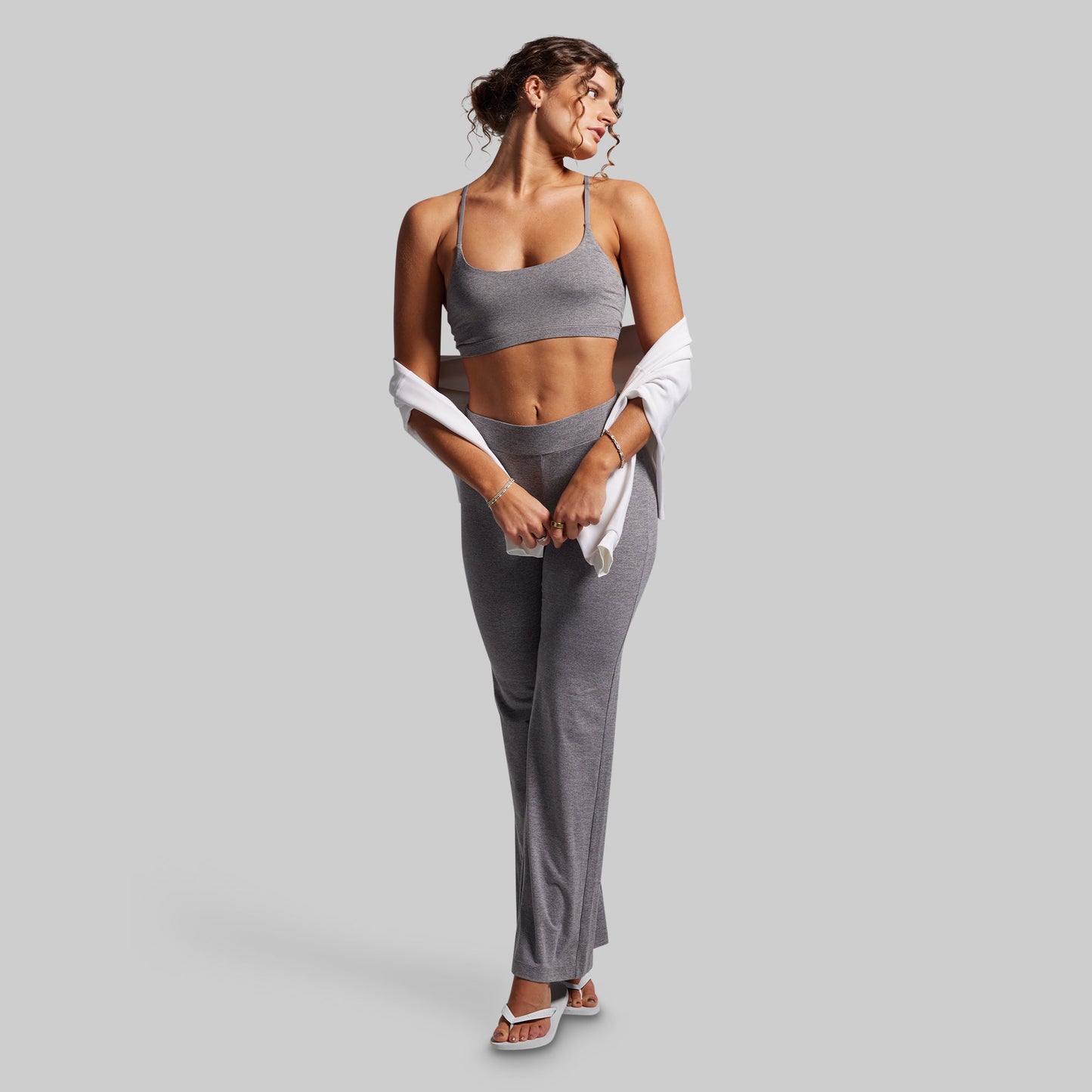 Woman in gray athletic wear holding a white sweatshirt on a light gray background