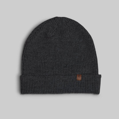 A dark charcoal gray ribbed knit beanie hat with a folded cuff and a small brown leather logo patch on the side, shown against a solid light gray background.