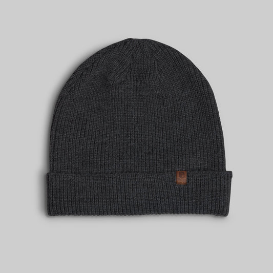 A dark charcoal gray ribbed knit beanie hat with a folded cuff and a small brown leather logo patch on the side, shown against a solid light gray background.