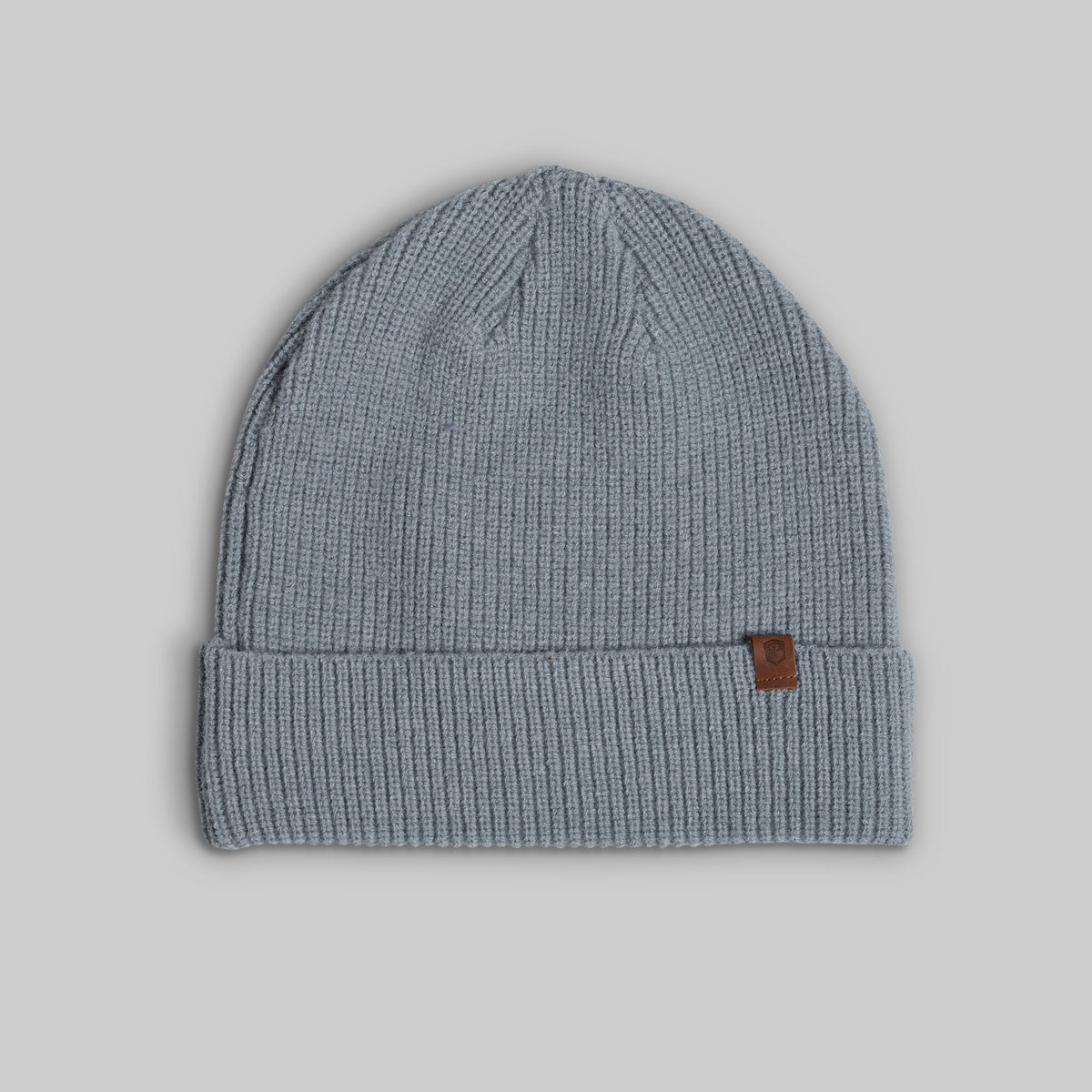 A light blue-gray ribbed knit beanie hat with a small brown leather brand tab on the cuff, shown against a solid gray background.