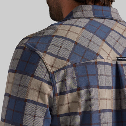 Close-up back view of a man wearing a plaid button-up shirt in blue, beige, and brown, with a small black brand tab on the upper right shoulder.
