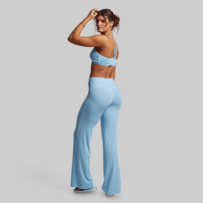Woman wearing a light blue sports bra and high-waisted wide- leg pants on a gray background