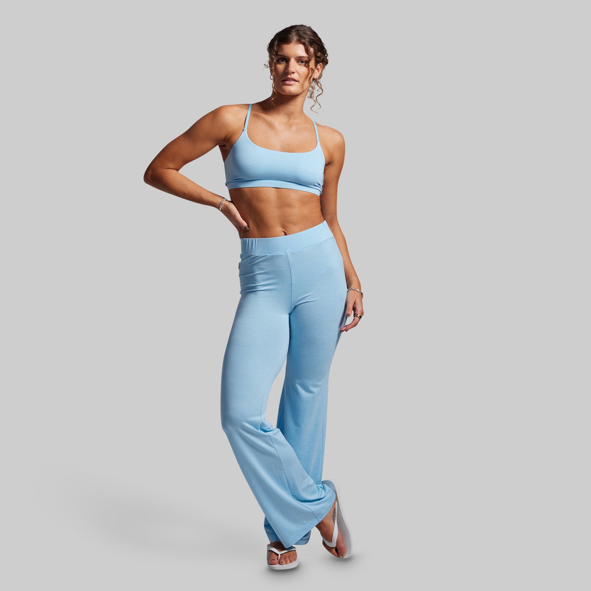 Woman wearing a light blue sports bra and high-waisted wide- leg pants on a gray background