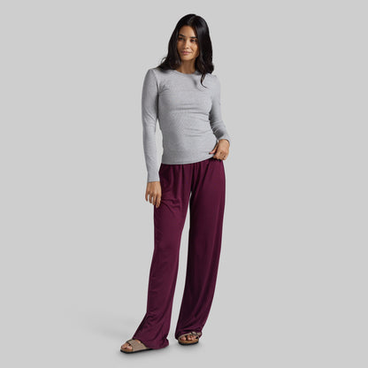 A woman modeling a light gray long-sleeve top and burgundy wide-leg pants against a solid gray studio background.