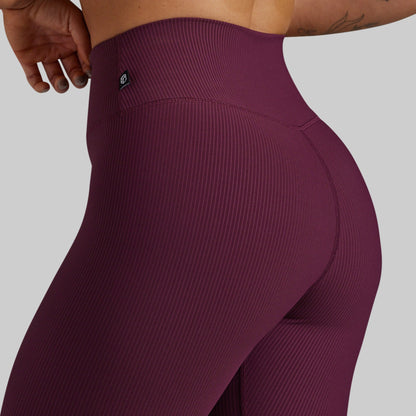Close-up of a model wearing ribbed high-waisted leggings in a deep plum purple color, showing the side and back fit against a solid gray background.