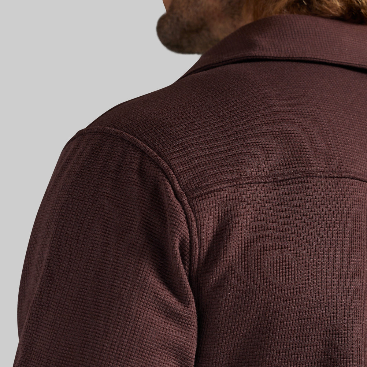 Close-up of a man wearing a textured waffle-knit jacket in a deep burgundy brown, showing the back of the neck and shoulder against a light gray background.