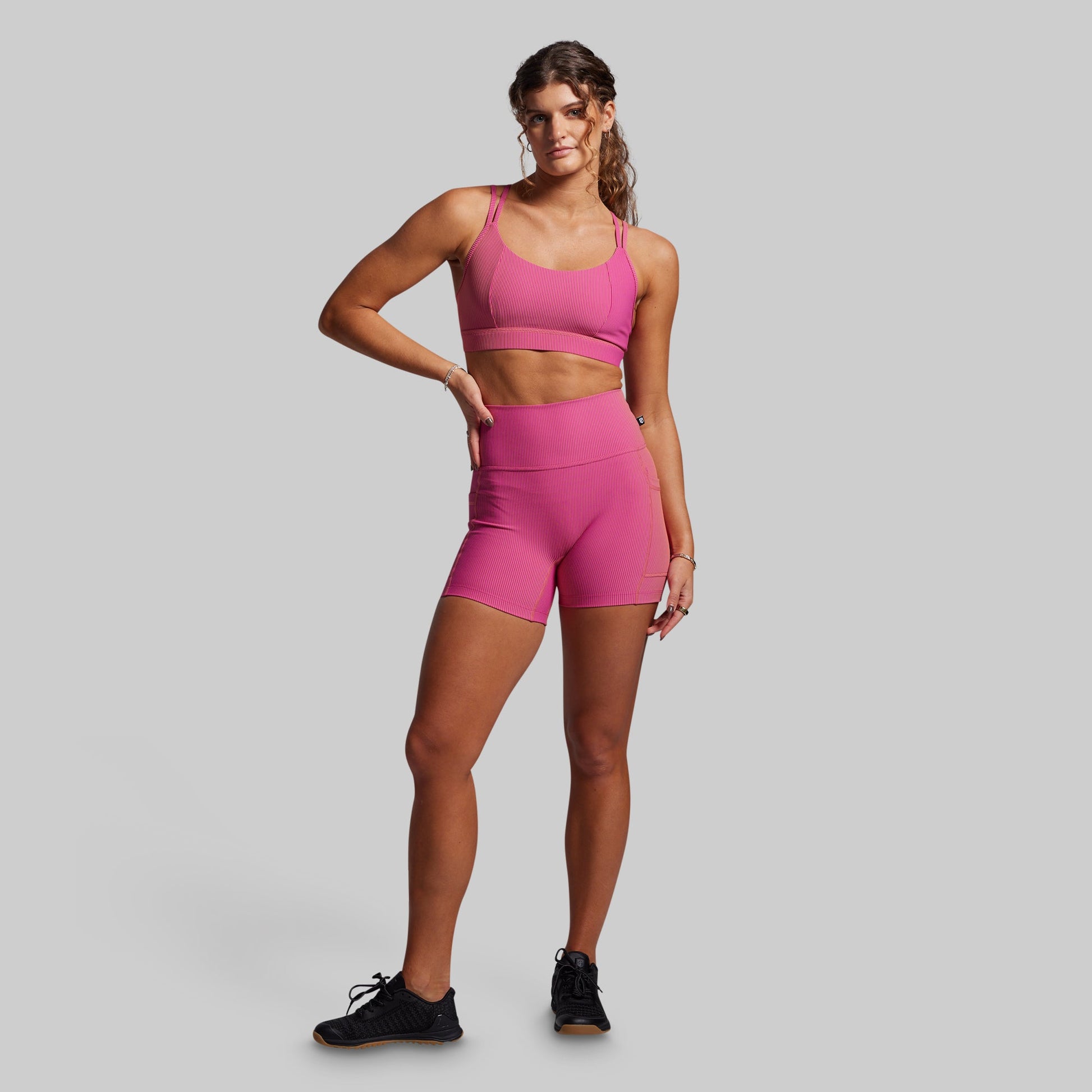 Woman wearing a pink ribbed athletic outfit on a gray background