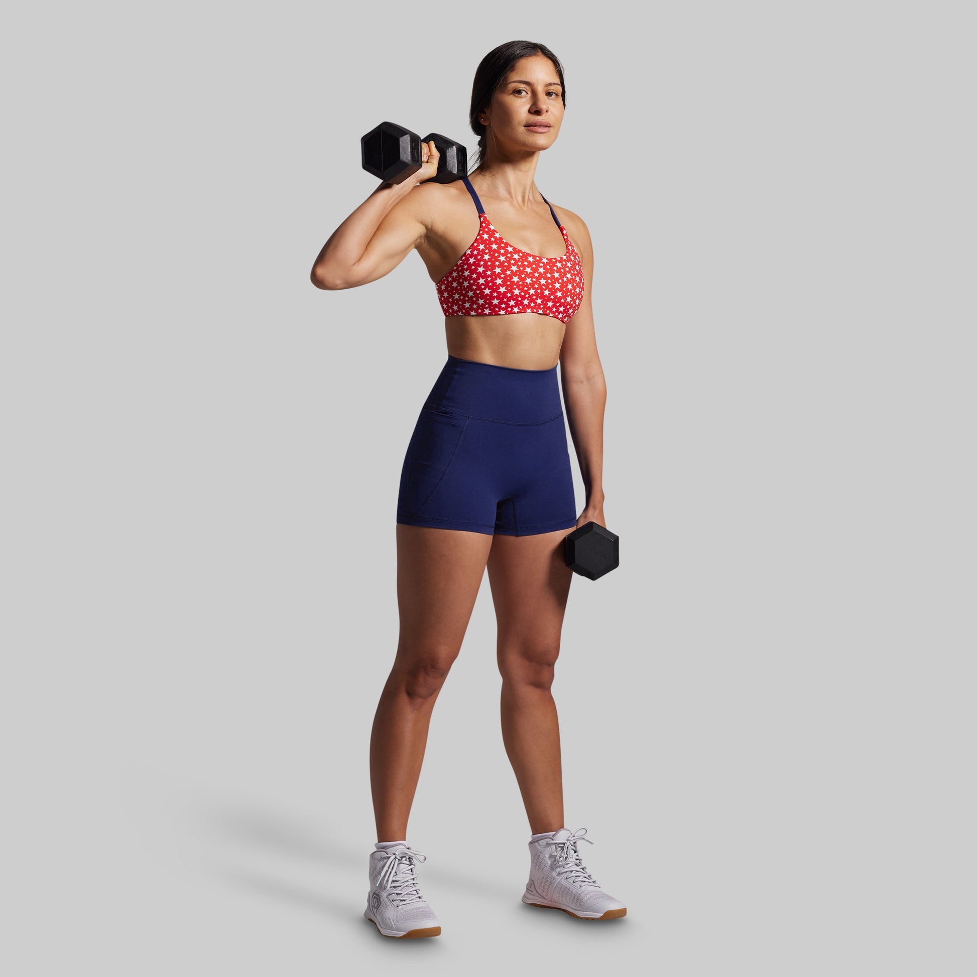 Woman in athletic wear holding dumbbells against a plain background