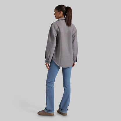 A woman shown from the back wearing a heather gray button-up jacket and light blue jeans, standing against a solid light gray studio background.