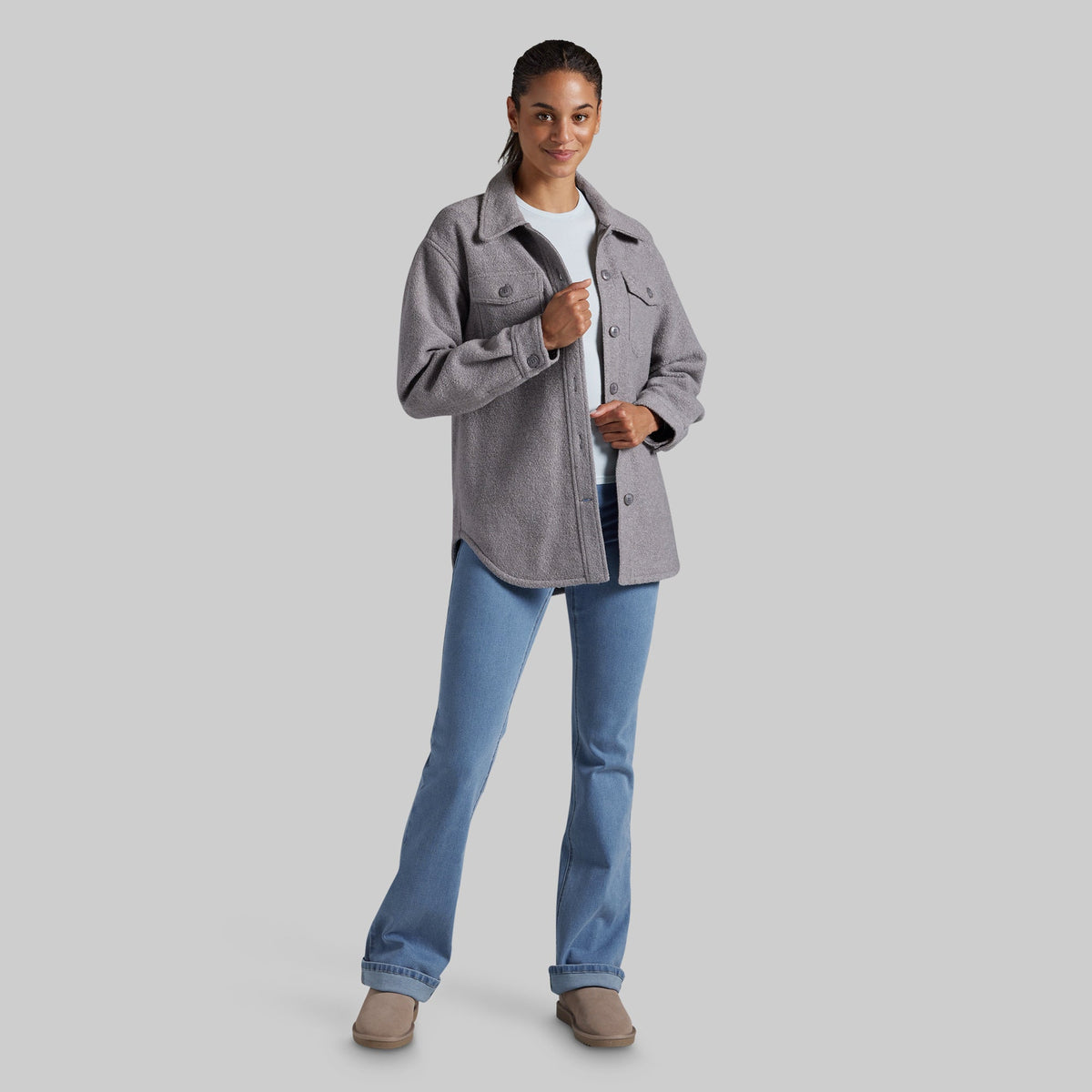A woman modeling a heather gray button-up jacket over a white t-shirt and blue jeans, standing against a solid gray studio background.