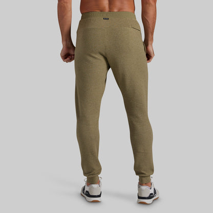 A man wearing textured olive green jogger pants, shown from the back against a solid gray studio background.
