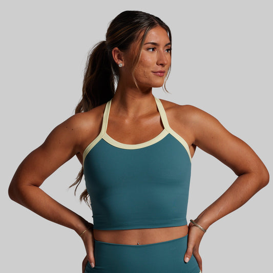 Woman wearing a teal sports bra and leggings with a yellow trim on sports bra on a gray background