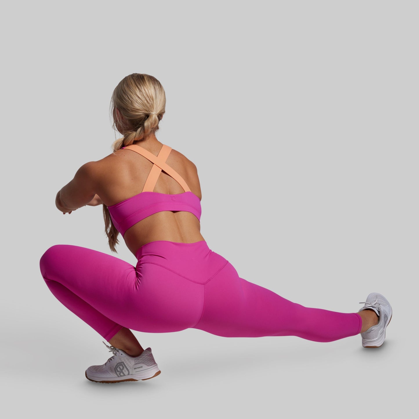 Woman in pink athletic outfit performing a lunge on a gray background