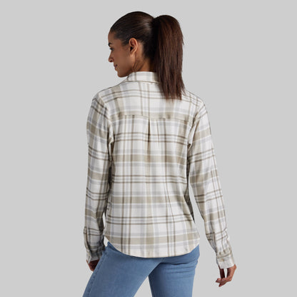 A woman shown from the back wearing a long-sleeve plaid button-up shirt in beige, white, and brown tones, paired with blue jeans, against a solid gray background.