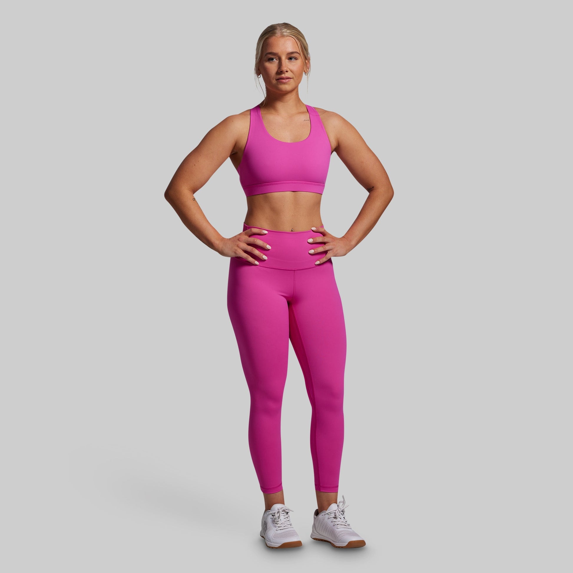 Woman wearing a pink sports bra and leggings set on a gray background