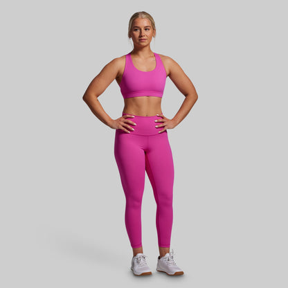 Woman wearing a pink sports bra and leggings set on a gray background