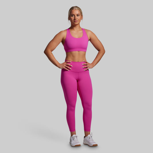 Woman wearing a pink sports bra and leggings set on a gray background