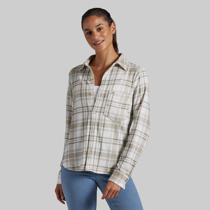 A woman modeling a long-sleeve plaid button-up shirt in beige, white, and light brown tones, paired with blue jeans, against a solid gray background.