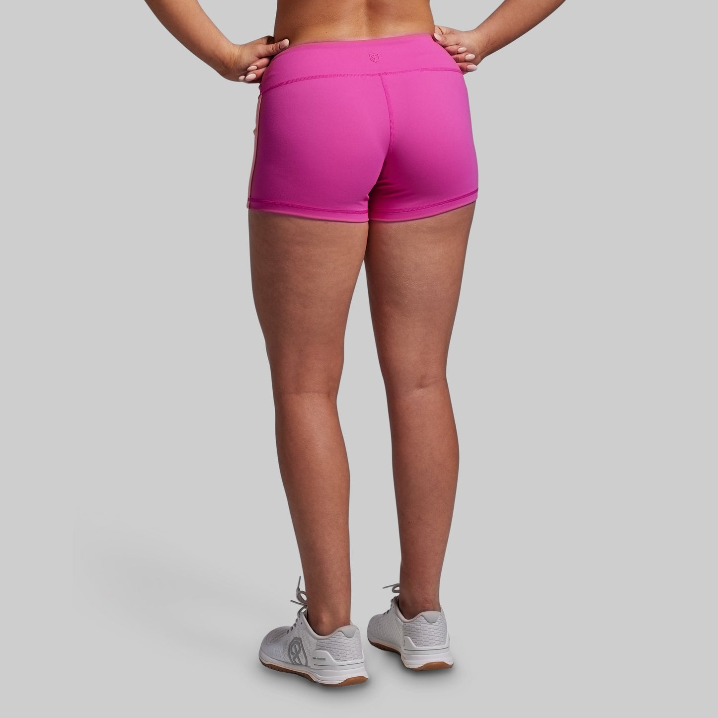 Person wearing bright pink athletic shorts on a gray background