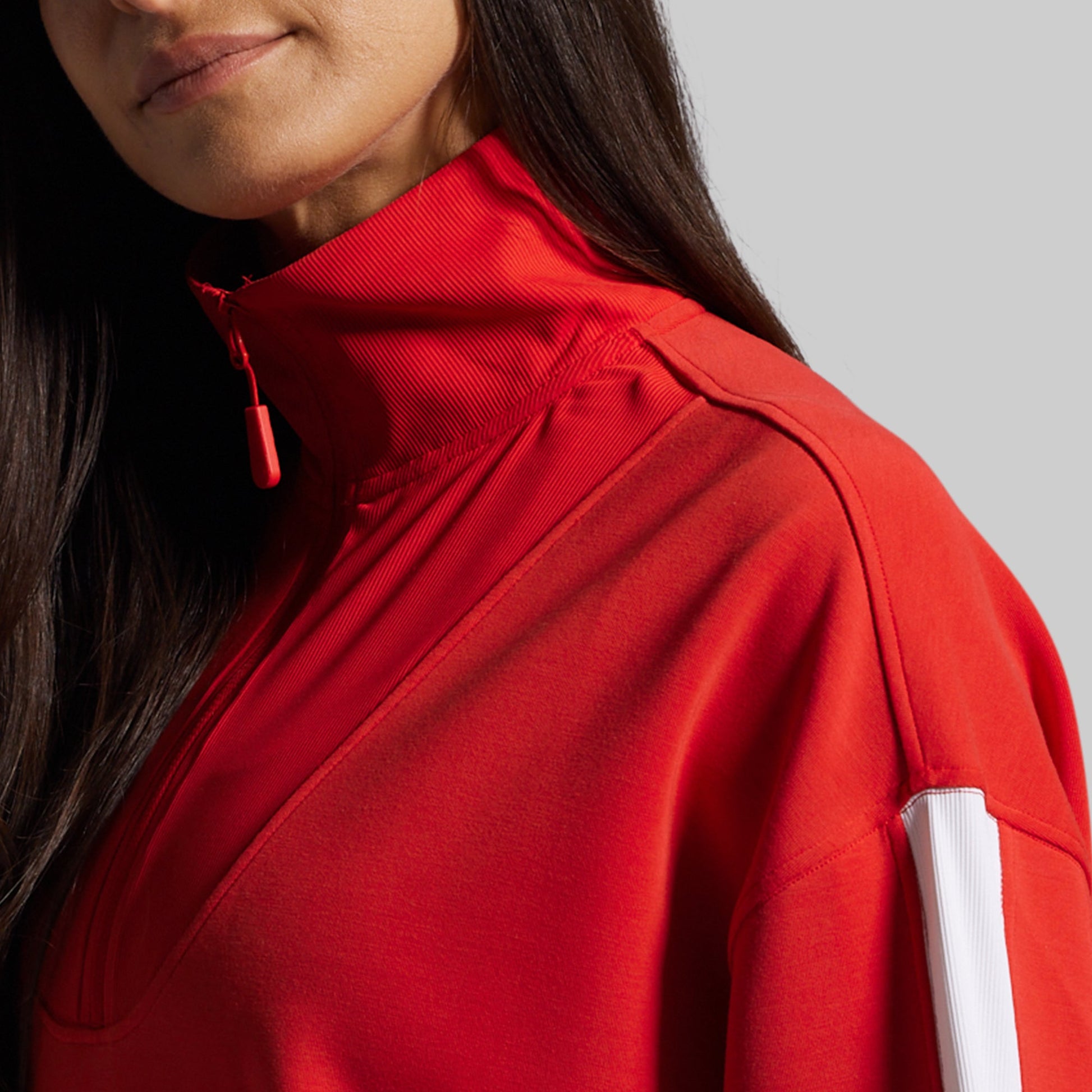 Person wearing a red jacket with a white stripe on a gray background