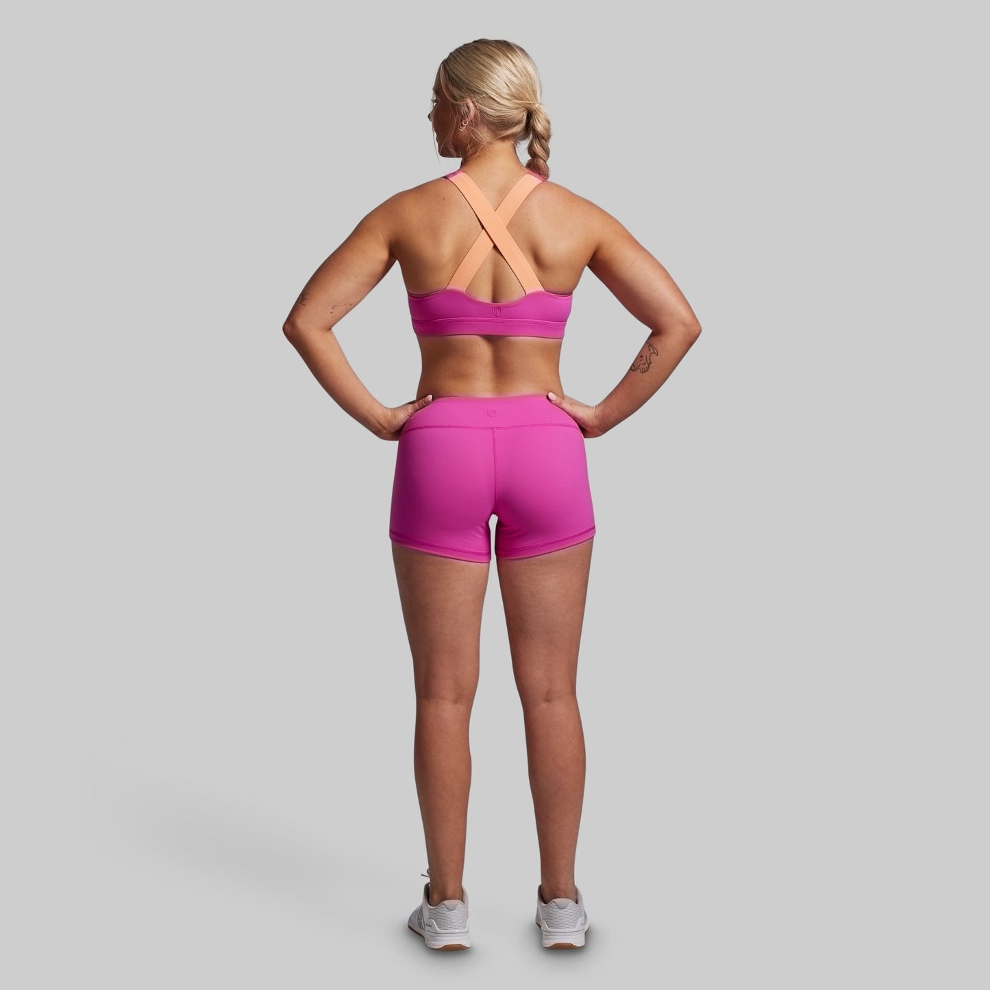 Woman wearing a pink sports bra and shorts on a gray background