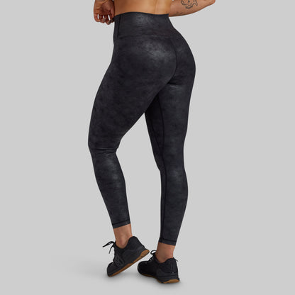 Rear three-quarter view of a model wearing high-waisted, full-length athletic leggings with a dark charcoal gray and black mottled texture, paired with black sneakers, against a solid light gray background.