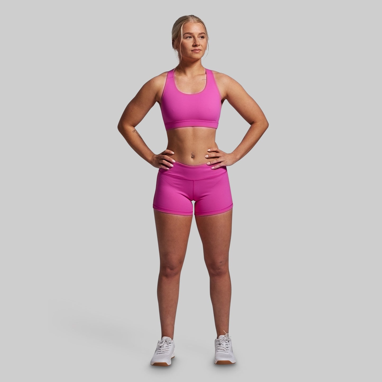 Woman wearing a pink sports bra and shorts set on a gray background