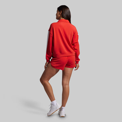 Woman wearing a red sweatshirt and shorts on a gray background