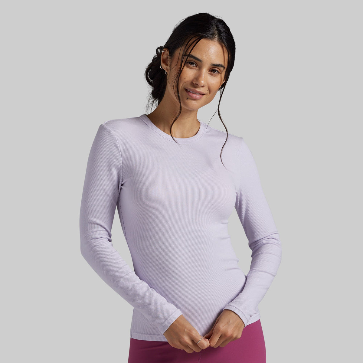 A woman modeling a light lavender long-sleeve athletic top against a solid gray studio background.