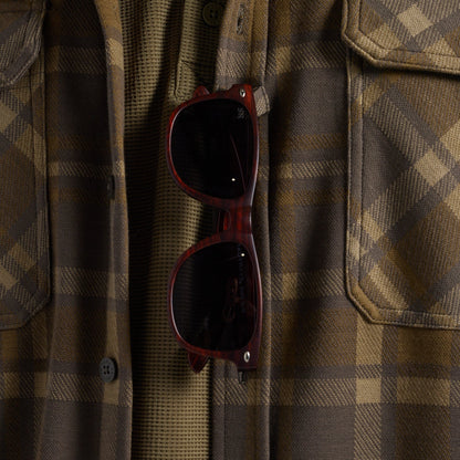 Close-up of sunglasses hanging from the sunglass loop of a brown and tan plaid flannel shirt.