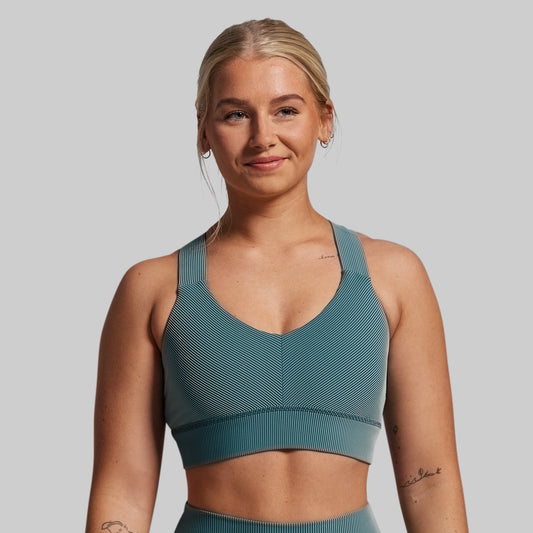 Woman wearing a teal sports bra and leggings against a plain background