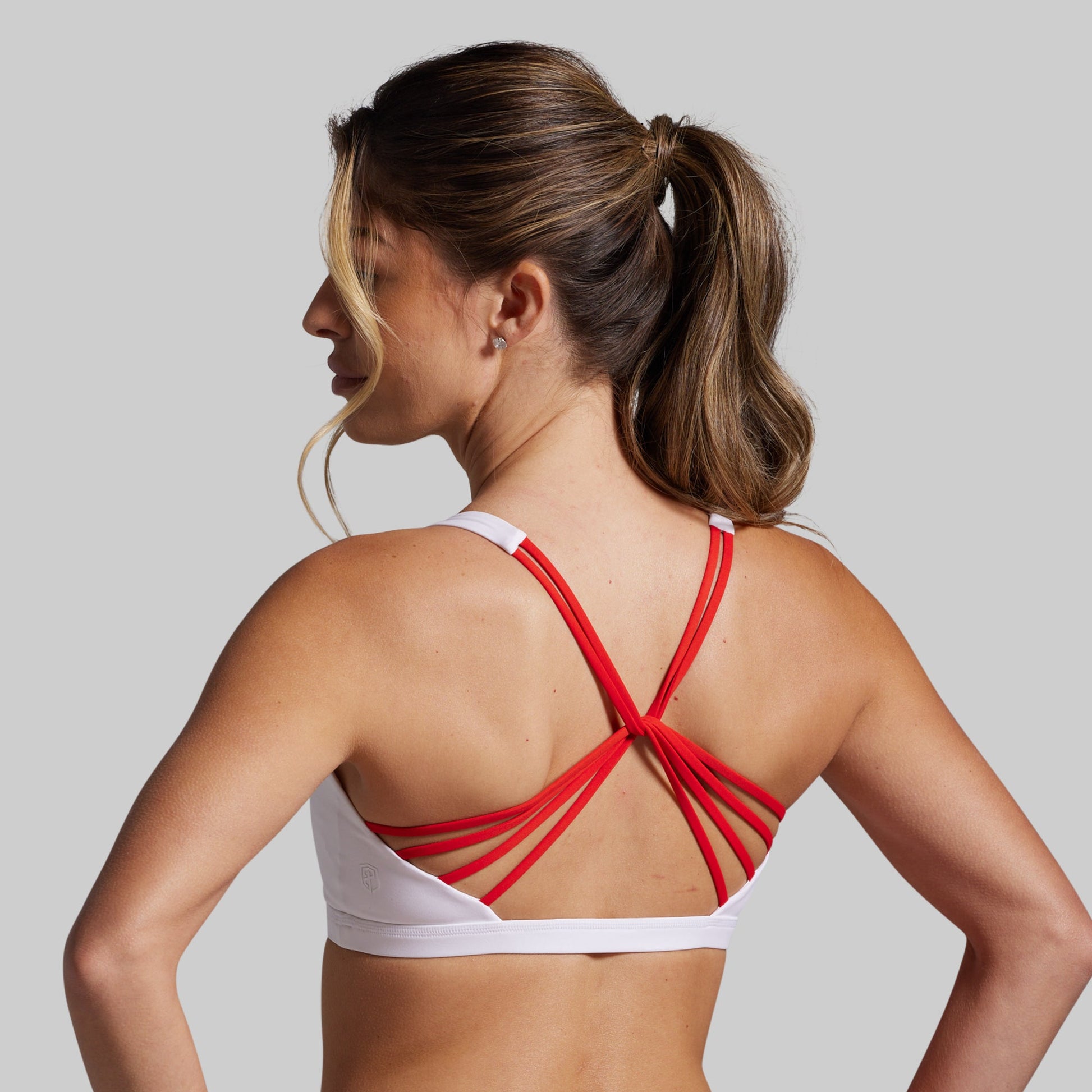 Woman wearing a white sports bra with red straps on a plain background