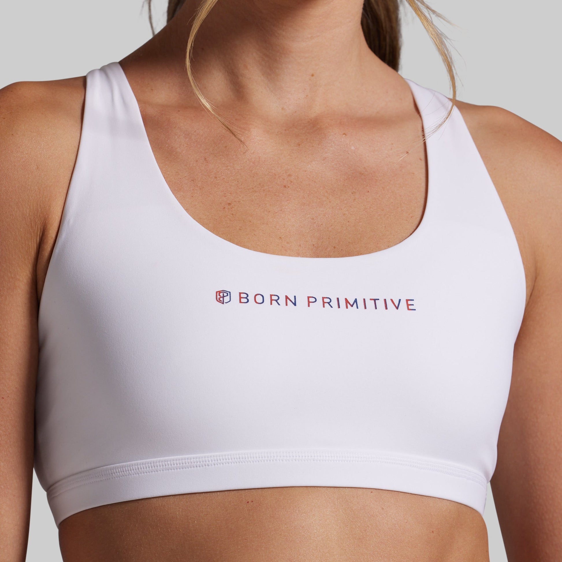 White sports bra with 'Born Primitive' logo on a neutral background